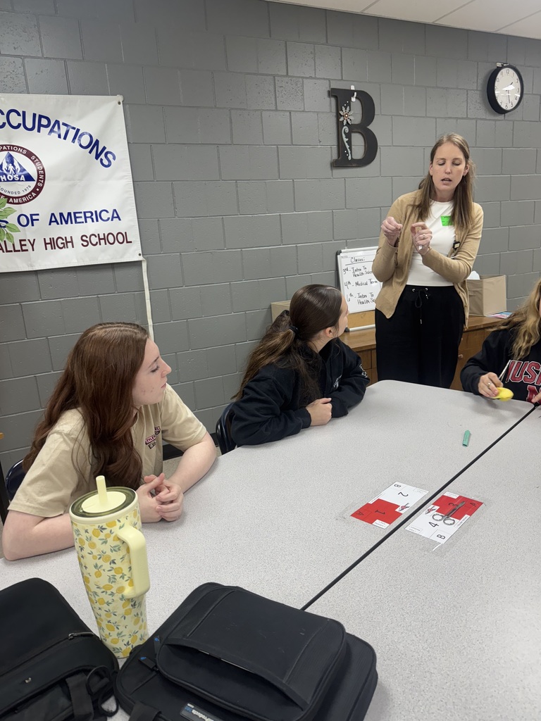 An instructor demonstrates a suturing technique to students seated at a table.