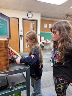 Two girls stand at a cart, working with a small lockbox.