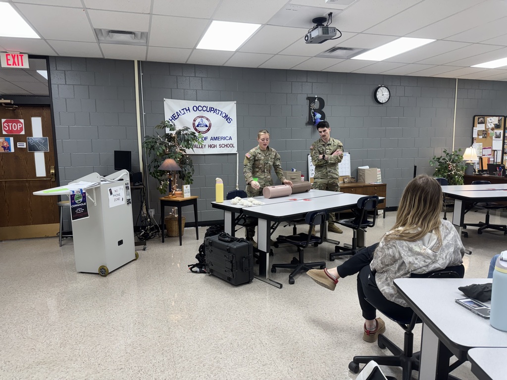 Two members of the Iowa Army National Guard demonstrate first aid techniques at the front of the classroom.