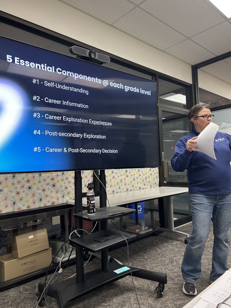 Close-up of a presenter next to a screen listing five essential components for each grade level.