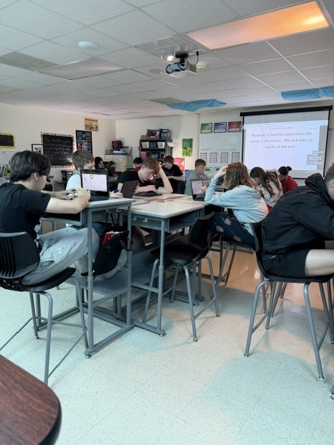 Students sitting in a classroom looking at a projector screen.