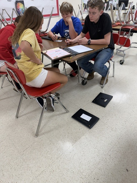 Three students discuss notes and assignments while working together at a cafeteria table.
