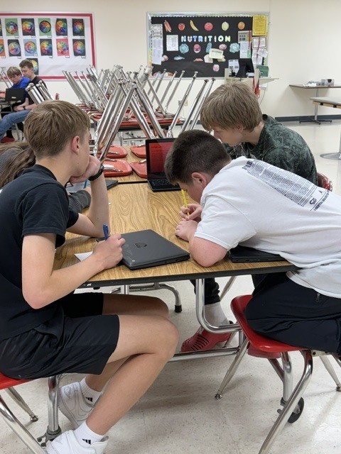 Three students review notes and work on a laptop together during a group learning activity.