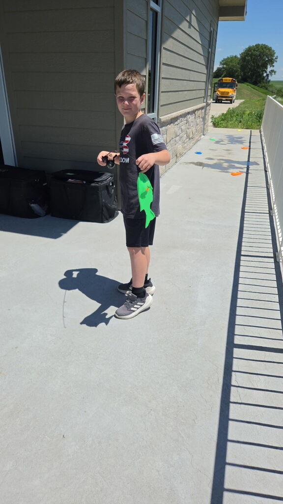Child in gray and green standing next to a fence.