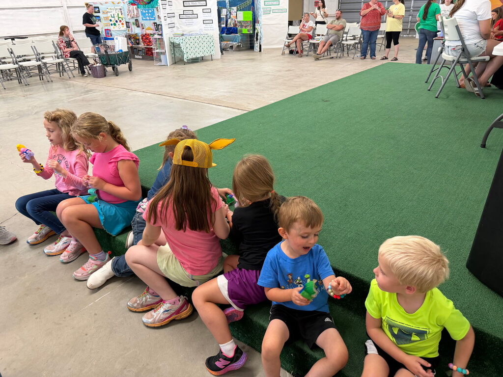 Kids sitting on the corner of a green rug.