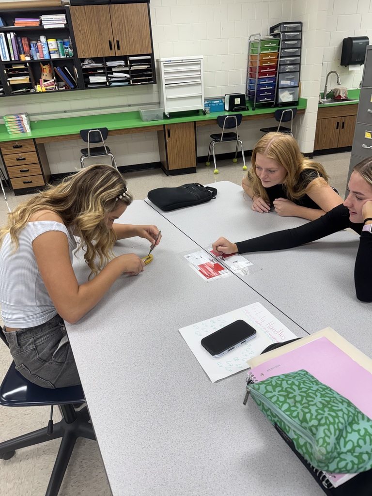 Three students work together at a table during a hands-on activity using bananas and small instruments.