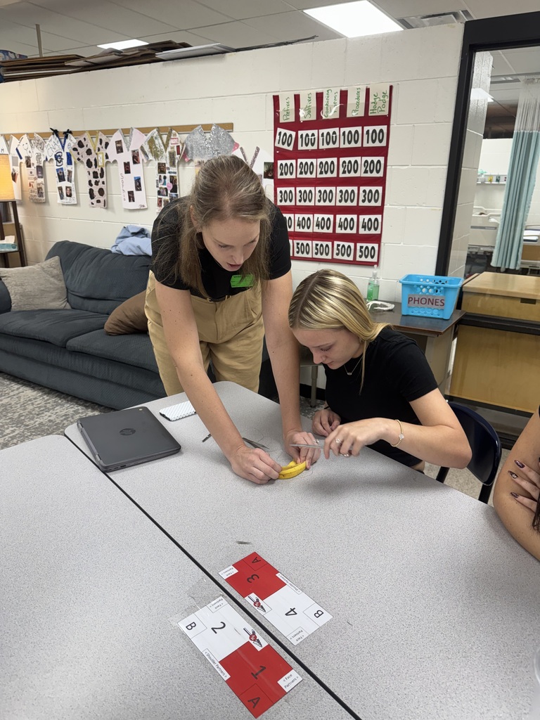 Instructor assists a seated student with a hands-on banana activity as classmates observe.