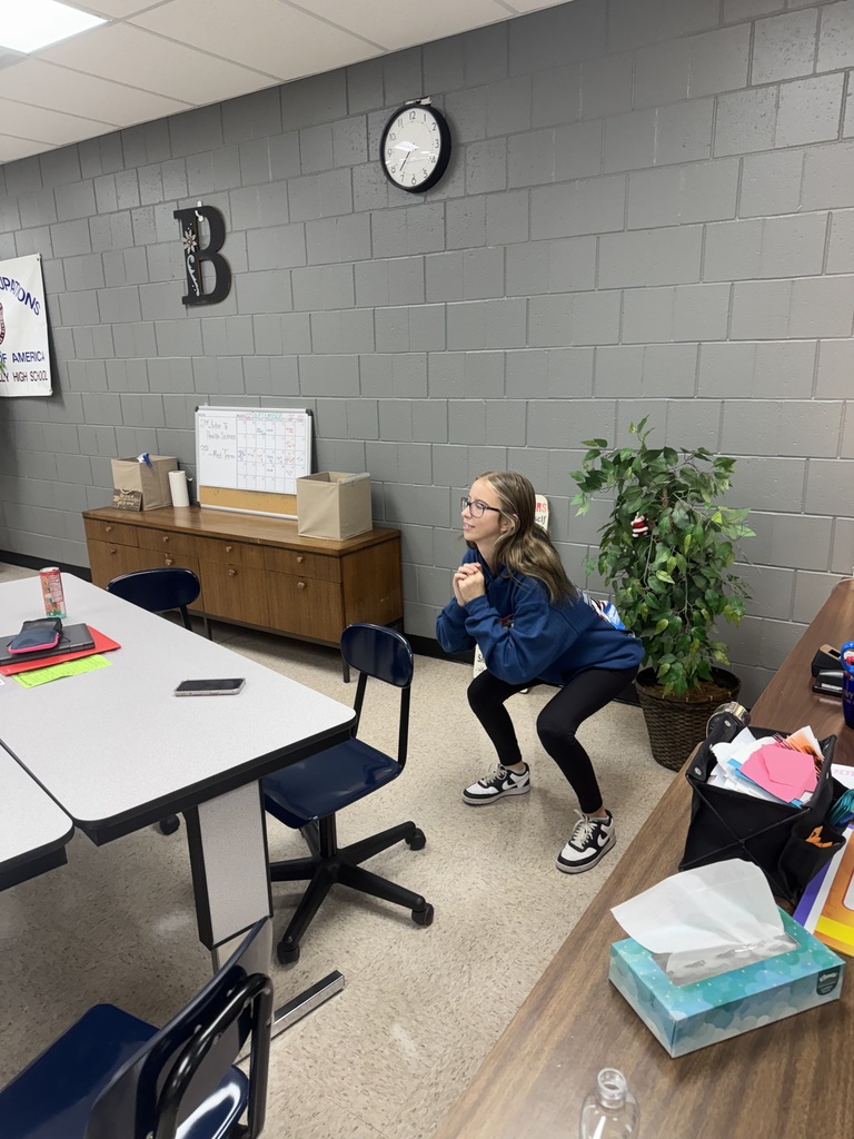 A student crouches with hands clasped while participating in a classroom activity.