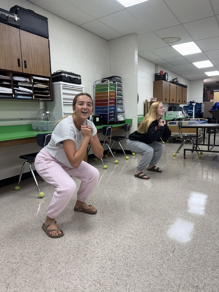 Two students crouch with hands clasped during an interactive classroom exercise.
