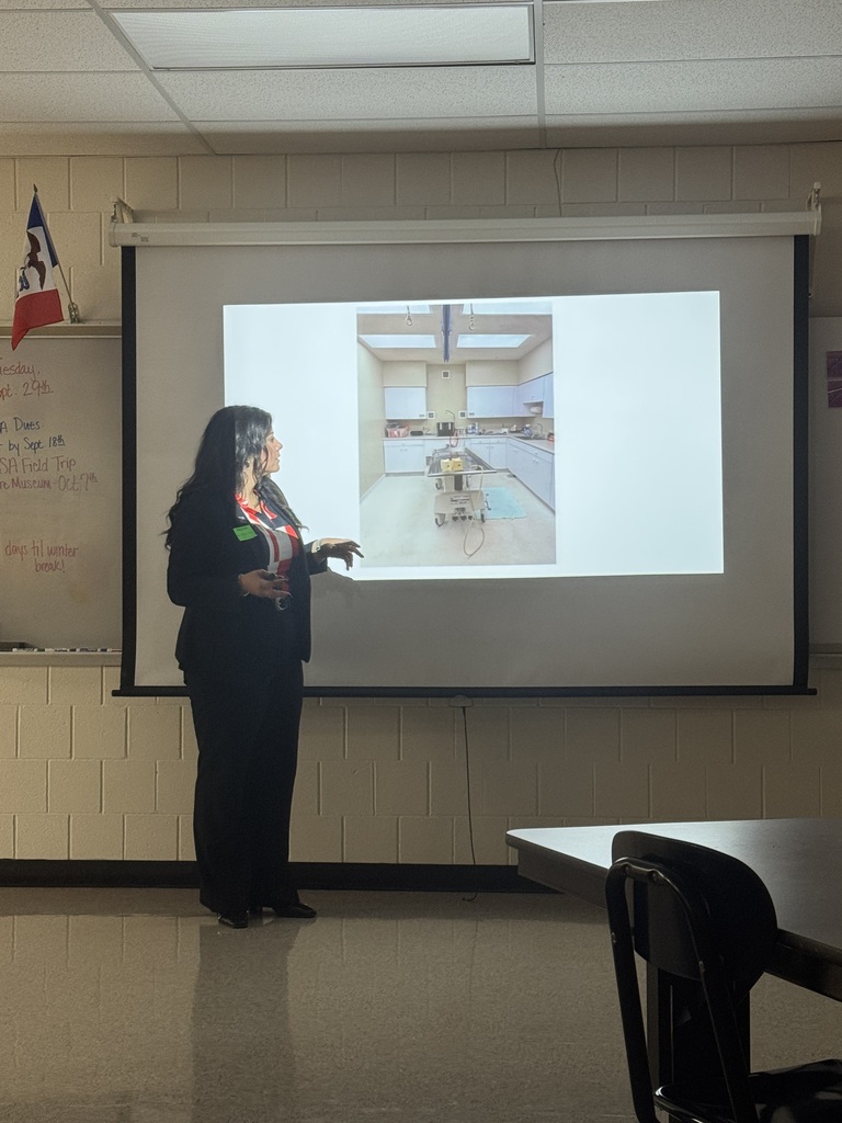 A funeral service professional presents a photograph of an embalming room on a classroom projection screen.
