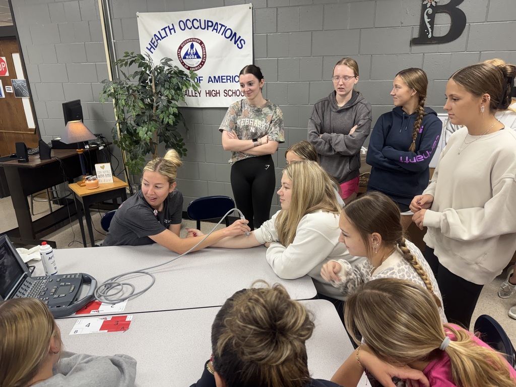 HOSA students watch as a healthcare professional demonstrates ultrasound imaging on a student's arm in the classroom.