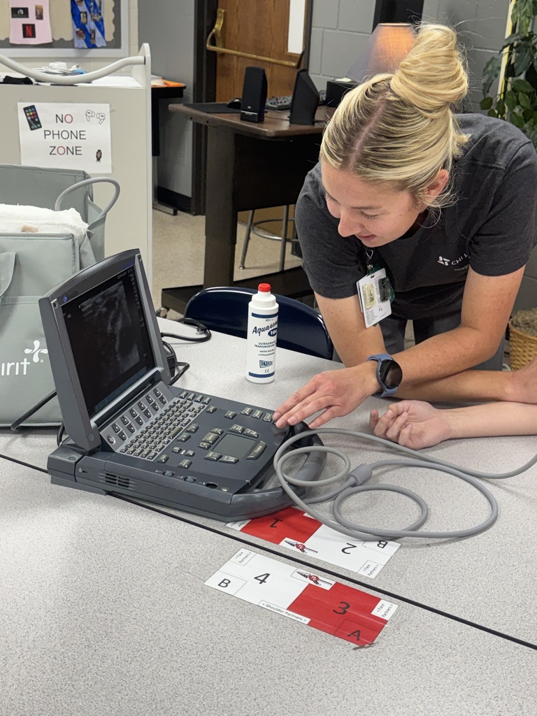 Healthcare professional demonstrates an ultrasound machine, displaying a scan on the screen during a classroom lesson.