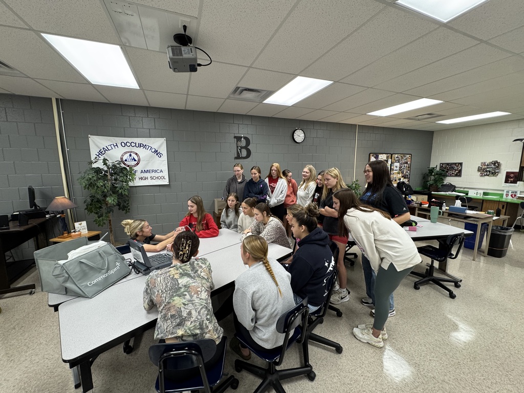 High school HOSA students gather around a table to watch a healthcare professional demonstrate ultrasound technology.