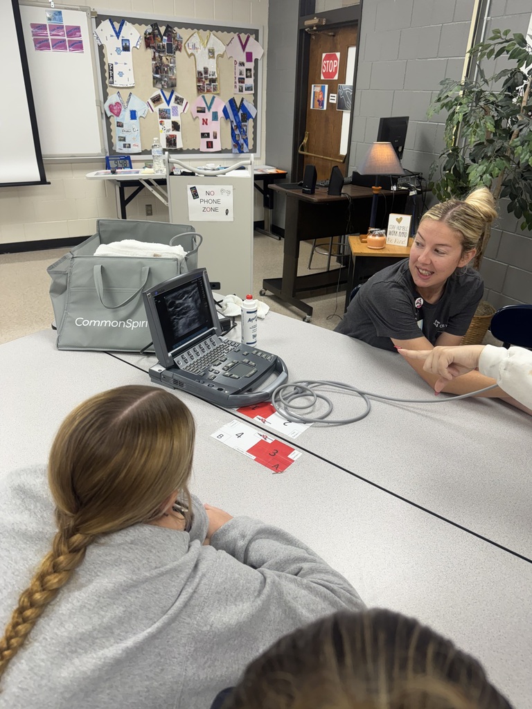 Healthcare professional explains an ultrasound scan to students gathered around a portable ultrasound machine.