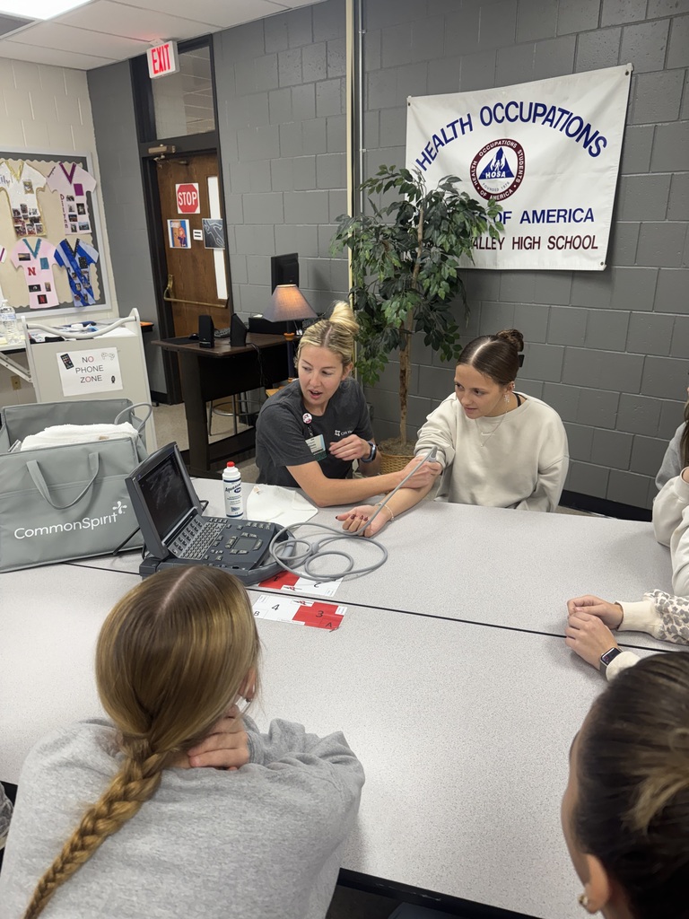 Healthcare professional uses an ultrasound probe on a student's arm as classmates observe during a hands-on demonstration.