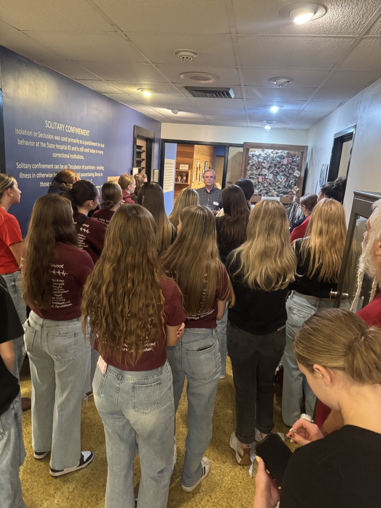 Students gather around a museum guide discussing solitary confinement in a hallway lined with historical exhibits.