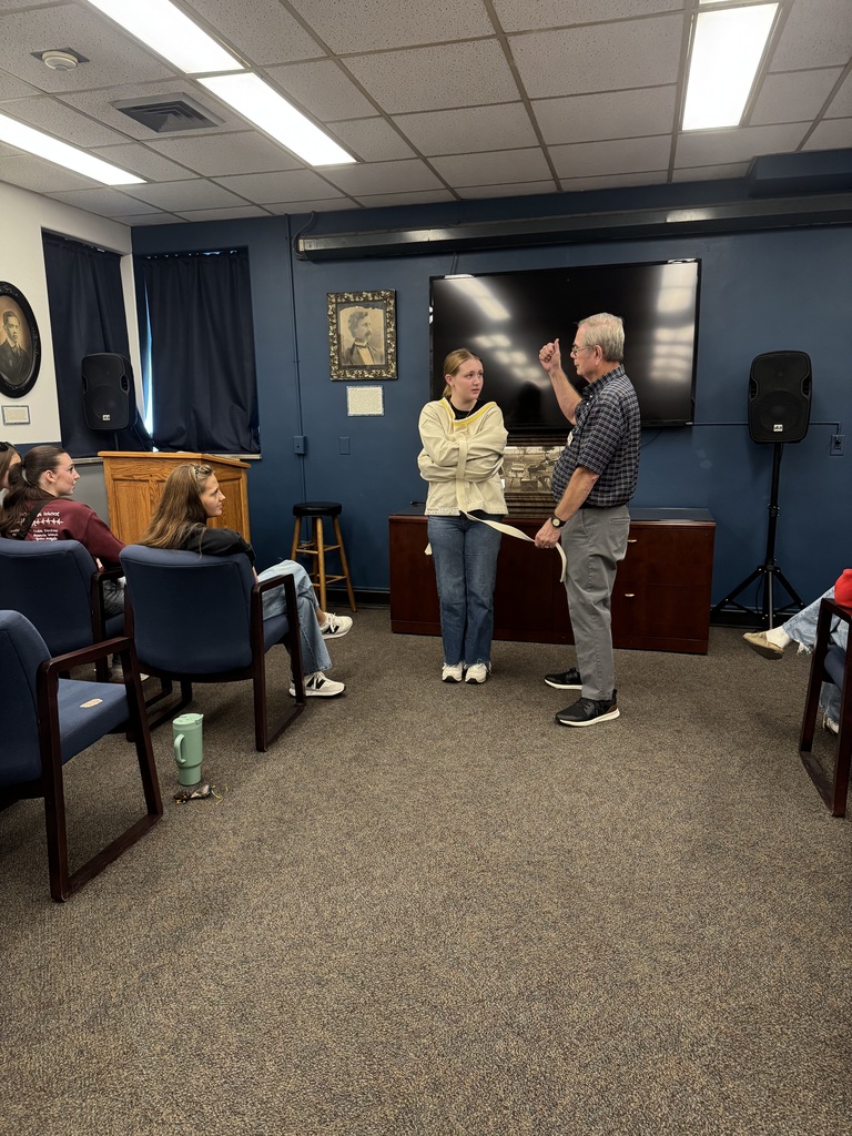 Museum guide demonstrates a historical restraint device with a student volunteer as classmates watch from their seats.