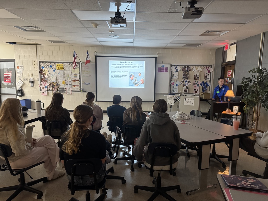 Students watch a dental professional present a “Dentistry 101” slideshow about oral health and dental care.