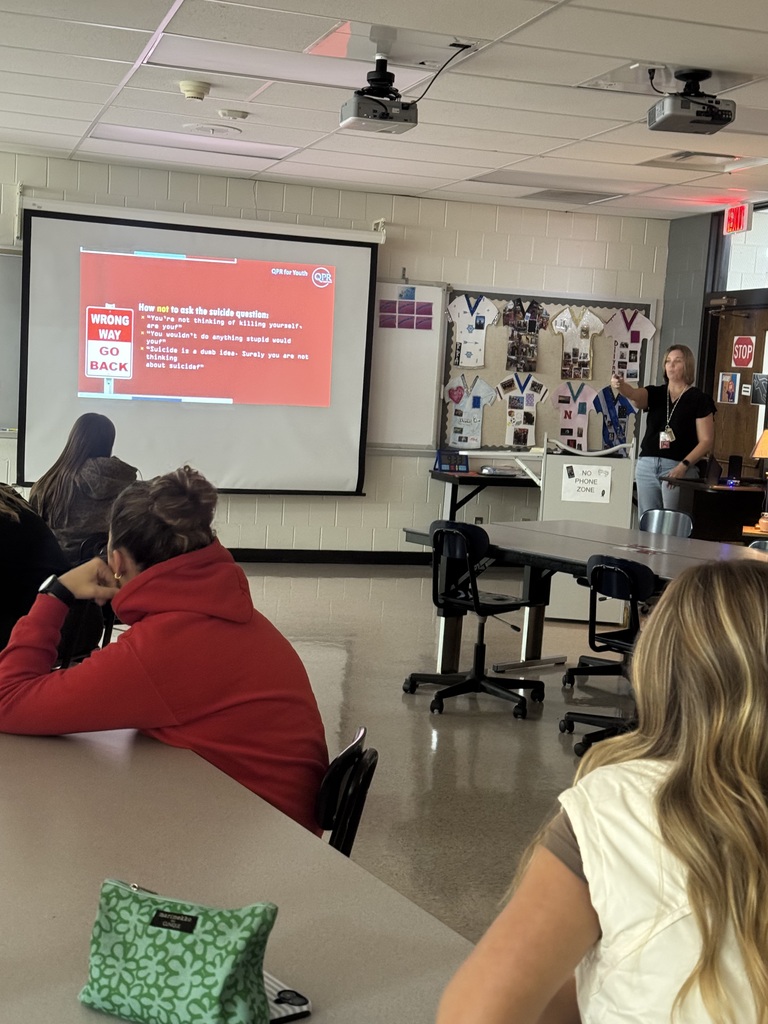 A presenter discusses suicide prevention with students while displaying a QPR slide about how not to ask suicide-related questions.