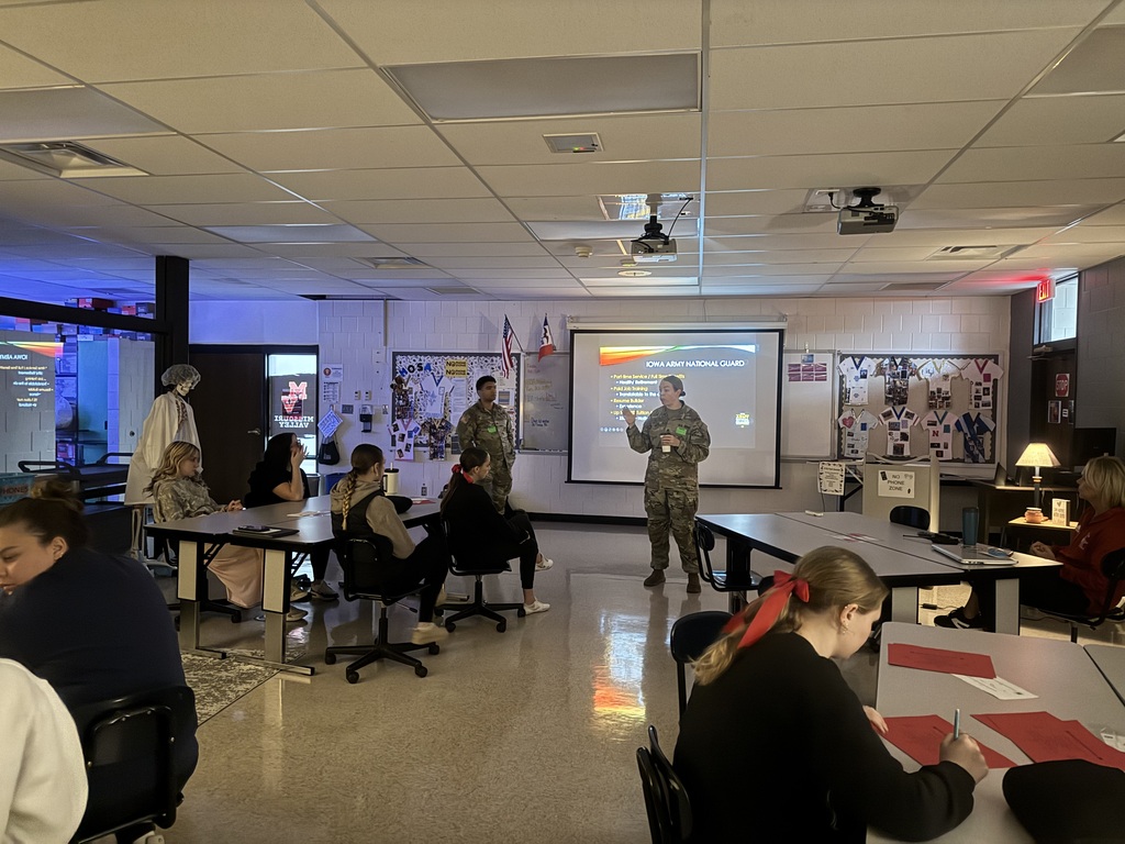 Two Iowa Army National Guard members in uniform present career opportunities to students seated in a classroom.