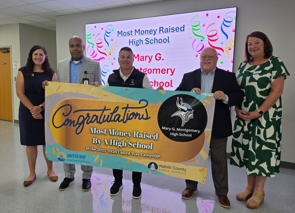 The Principal of Mary G. Montgomery High School, Mr. Diaz, standing with Dr. White, Mr. Dollar, and two representatives from United Way of Southwest Alabama as he receives a banner recognizing MGM as the high school who raised the most money for the campaign.