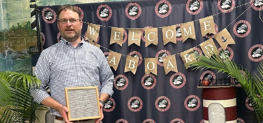 Principal holding first day of school sign.