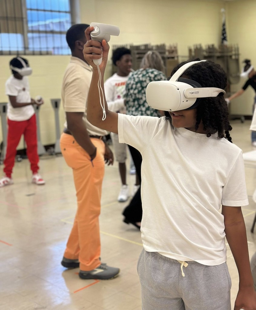 A student wears virtual reality goggles and holds a VR control stick