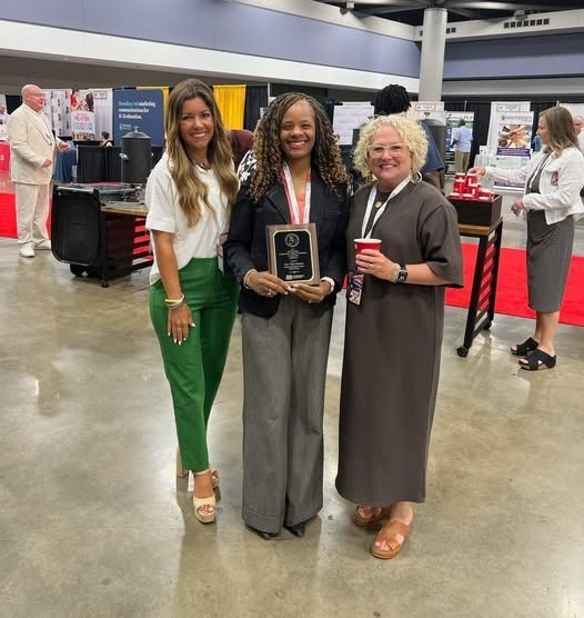 Assistant Principal Talia Johnson holds a plaque and stands with Hutchens Elementary Principal Brittney Owen and Dawes Intermediate Principal Mona Griffin