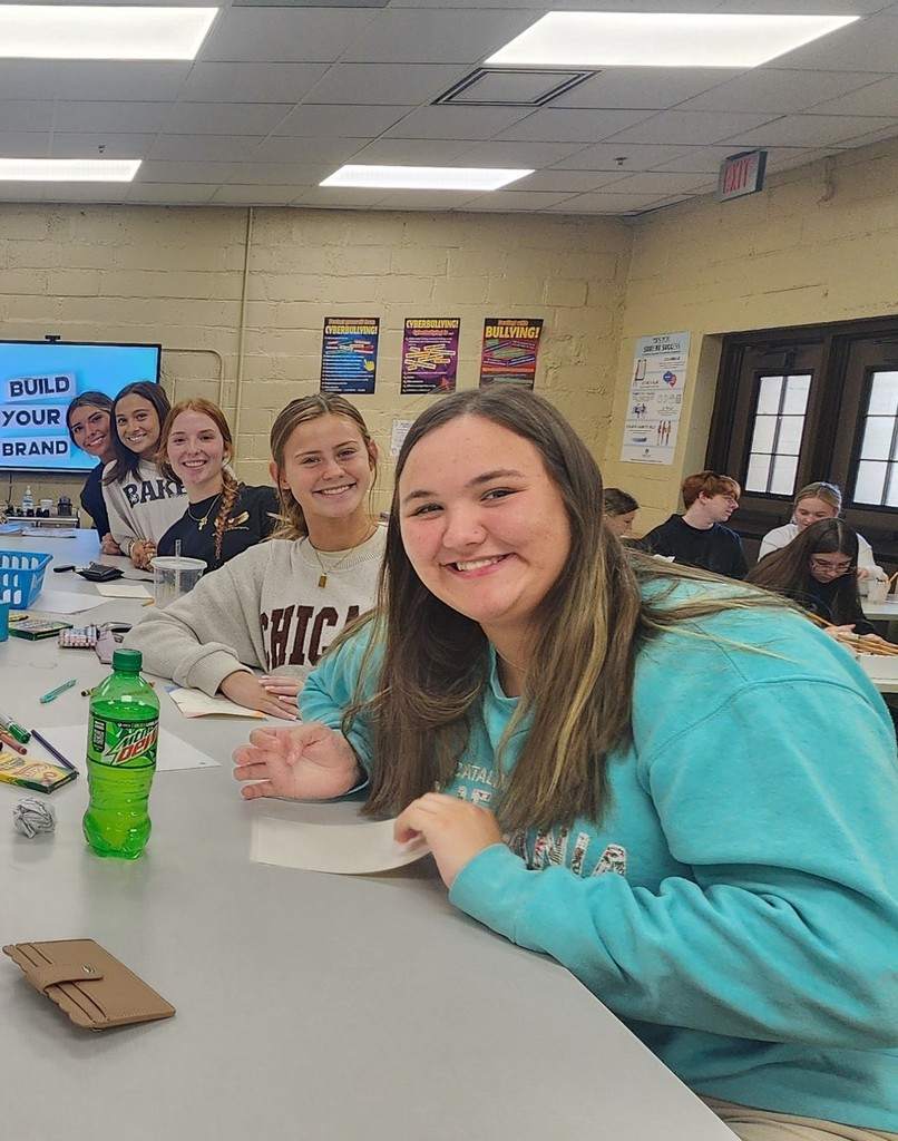 Five high school students smile while sitting at a table in a classroom