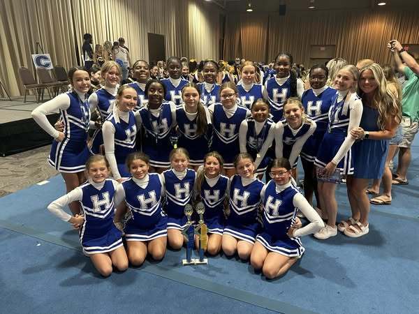 The Hankins Middle School cheerleaders, dressed in blue uniforms with an "H" on the front, pose for a group photo with their trophy