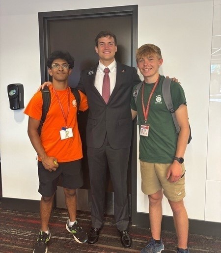 Two high school students in shorts and T-shirts stand with a man in a suit