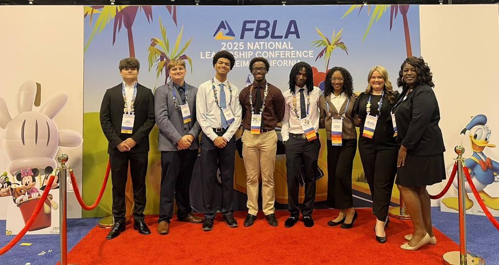 Several students and a teacher with nametags on lanyards around their necks, standing in front of a banner that reads: FBLA 2025 National Leadership Conference, Anaheim, California