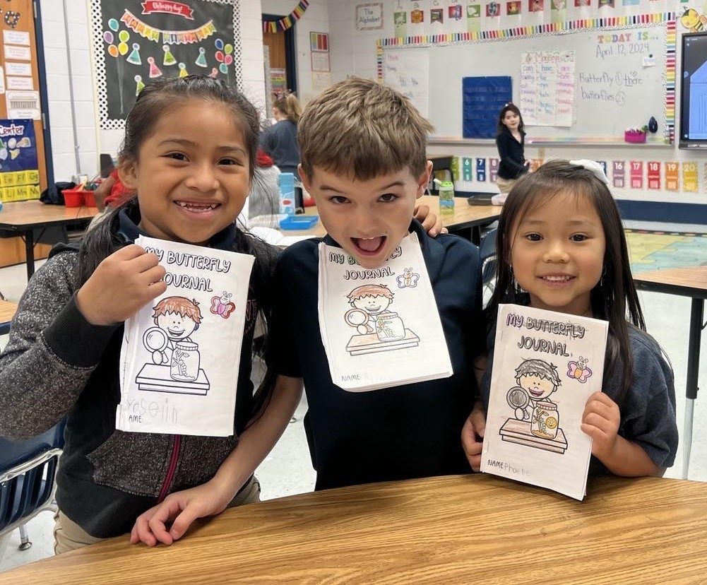 Three kindergarteners holding up booklets that read "My Butterfly Journal"