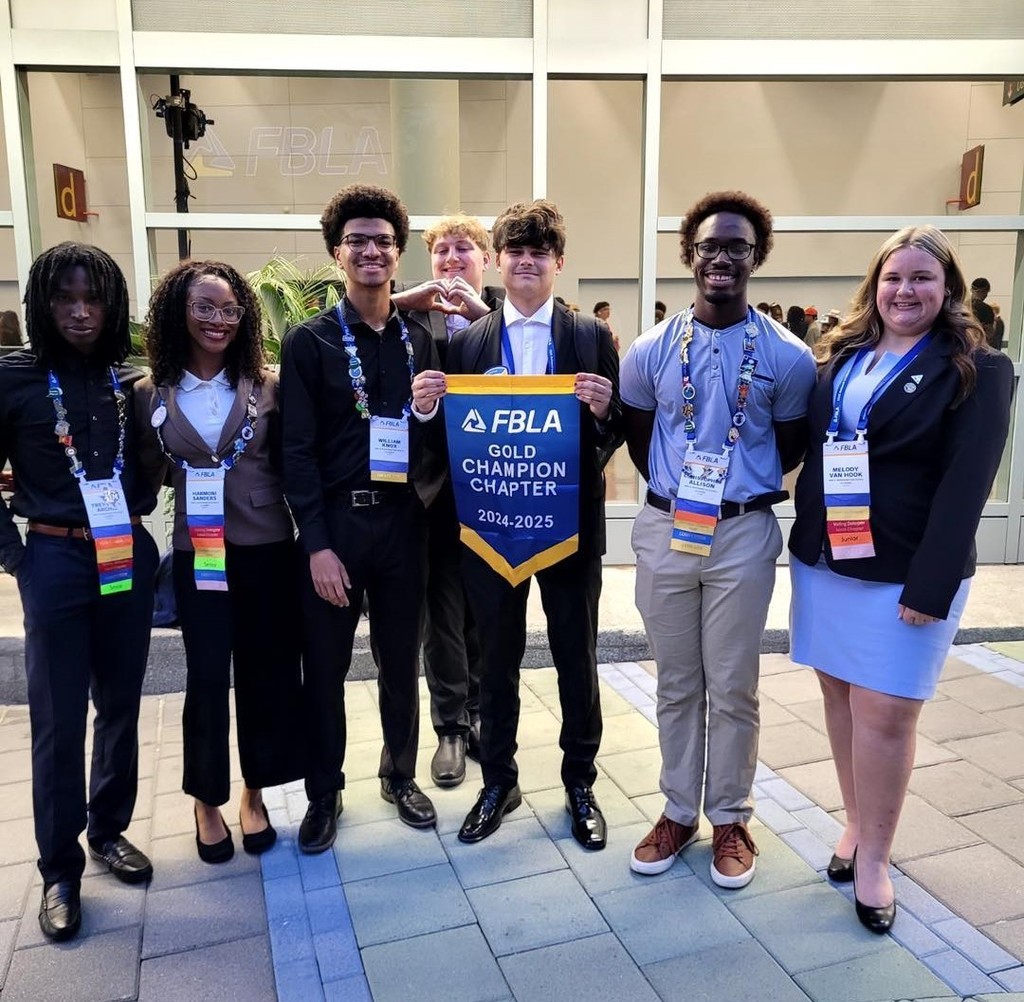 Seven students in blazers and lanyards, holding a small banner that reads: FBLA Gold Champion Chapter, 2024-25