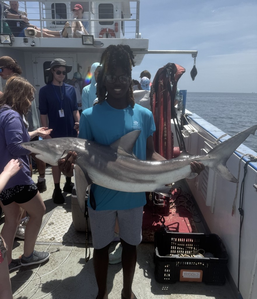 Jaylon Washigton holds a small shark on the deck of a boat