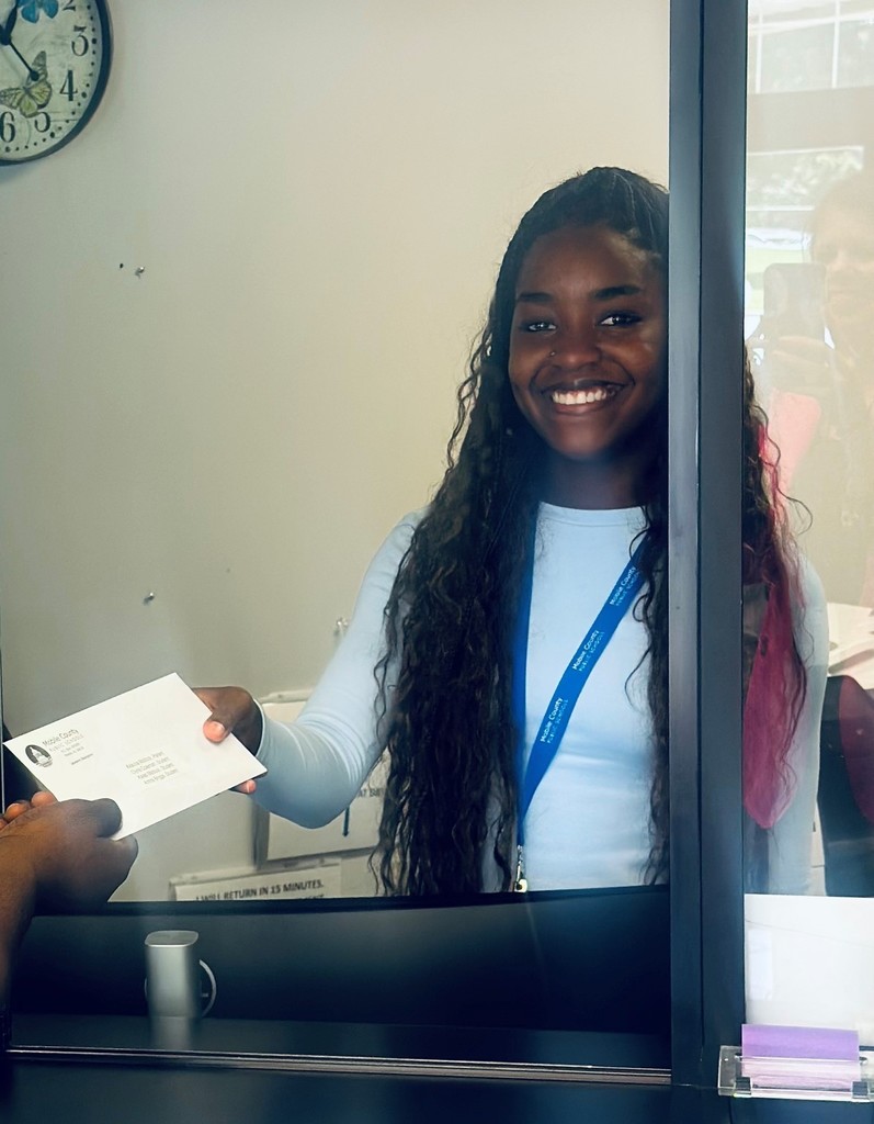 A smiling Aryn Williams hands a letter through a service window to someone on the other side