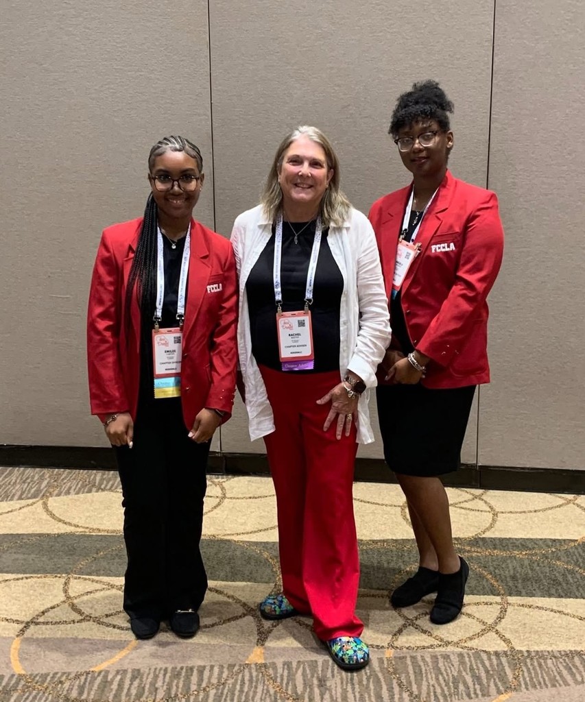 Two students in red blazers and lanyards and their instructor, Davidson culinary teacher Rachel Baxter