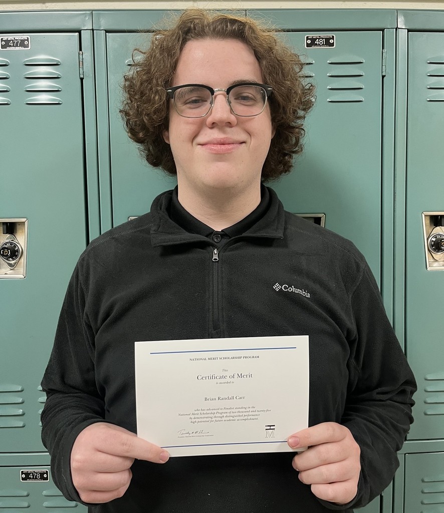Brian Carr holds a certificate, standing in front of lockers