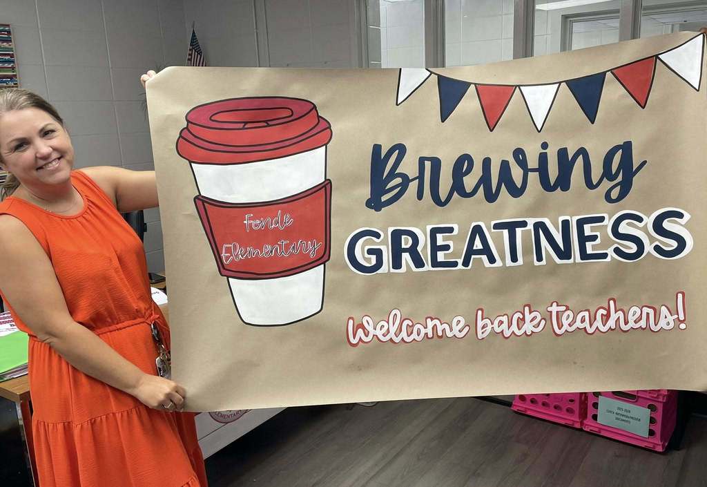 A teacher holds a banner that reads "Brewing Greatness: Welcome back teachers!"