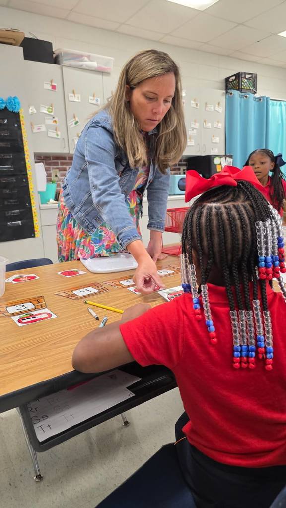 A teacher standing at a table, working with a student