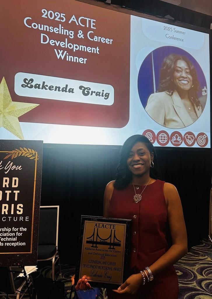 Lakenda Craig stands with her award beneath a photo of herself on a projector screen