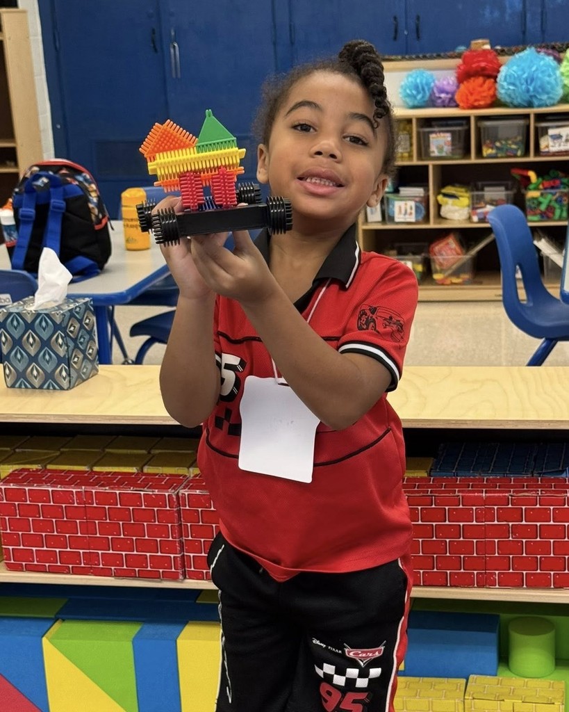 A preschool student holding up a house made of legos