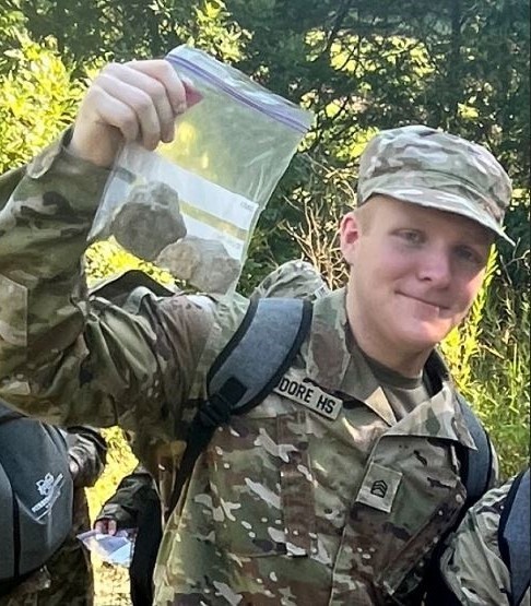 A JROTC cadet in camos holds a plastic bag filled with rocks
