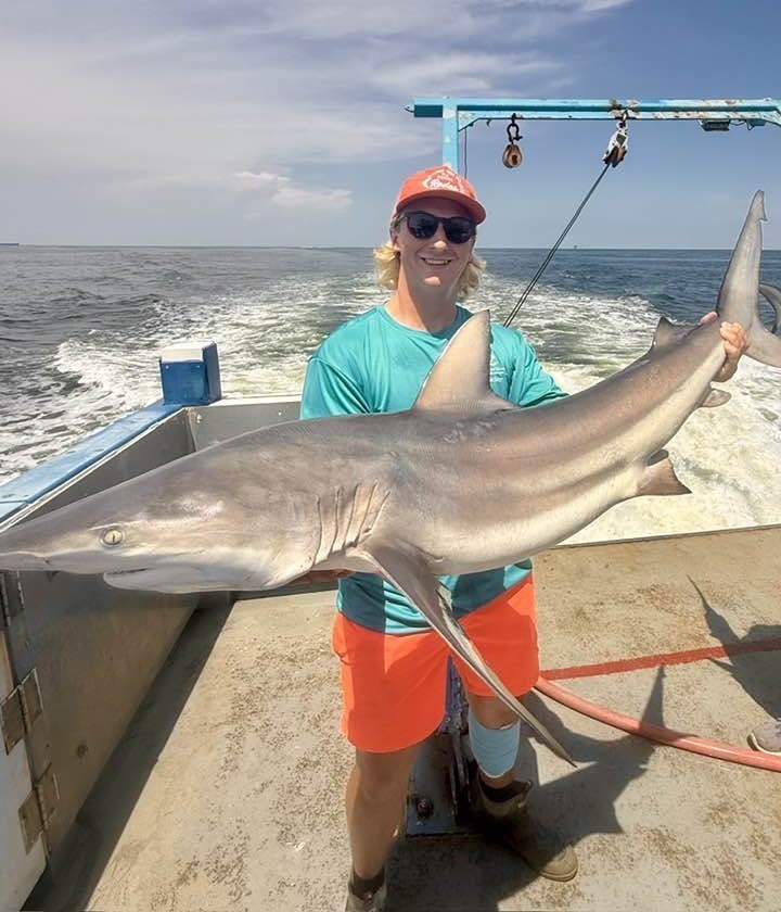Tucker Lewis, standing on a boat, holds a small shark