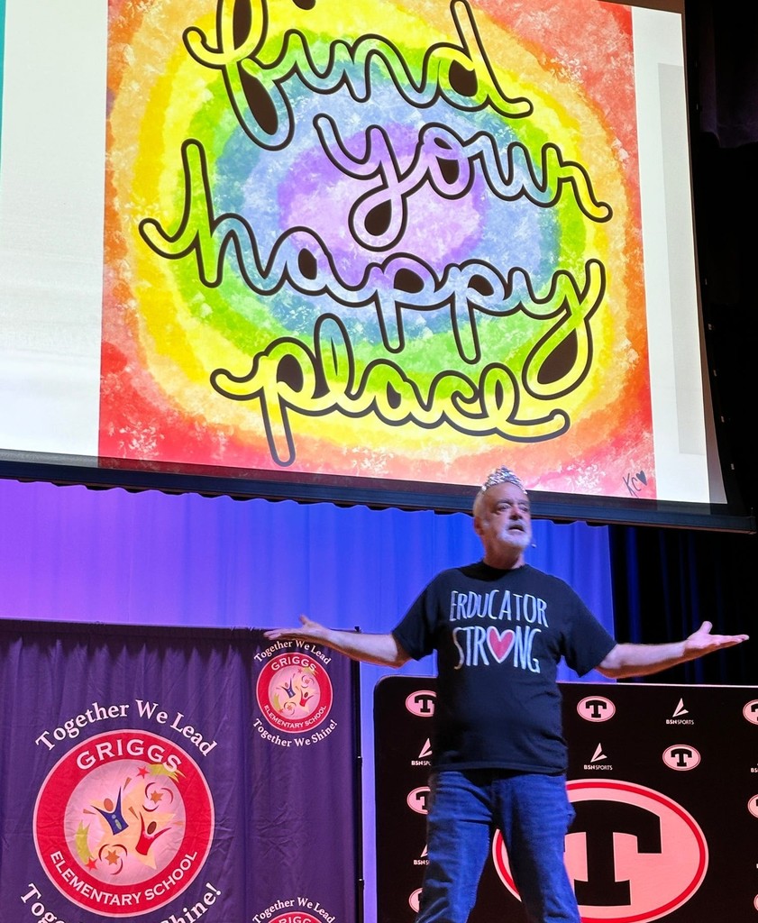 Gerry Brooks gestures on stage below a sign that reads "Find Your Happy Place"