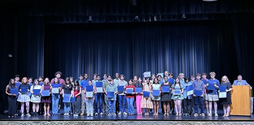A large group of students standing on a stage, holding certificates