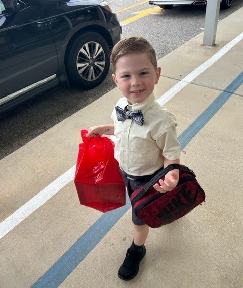 A boy in a bowtie walking with a bag and lunchbox