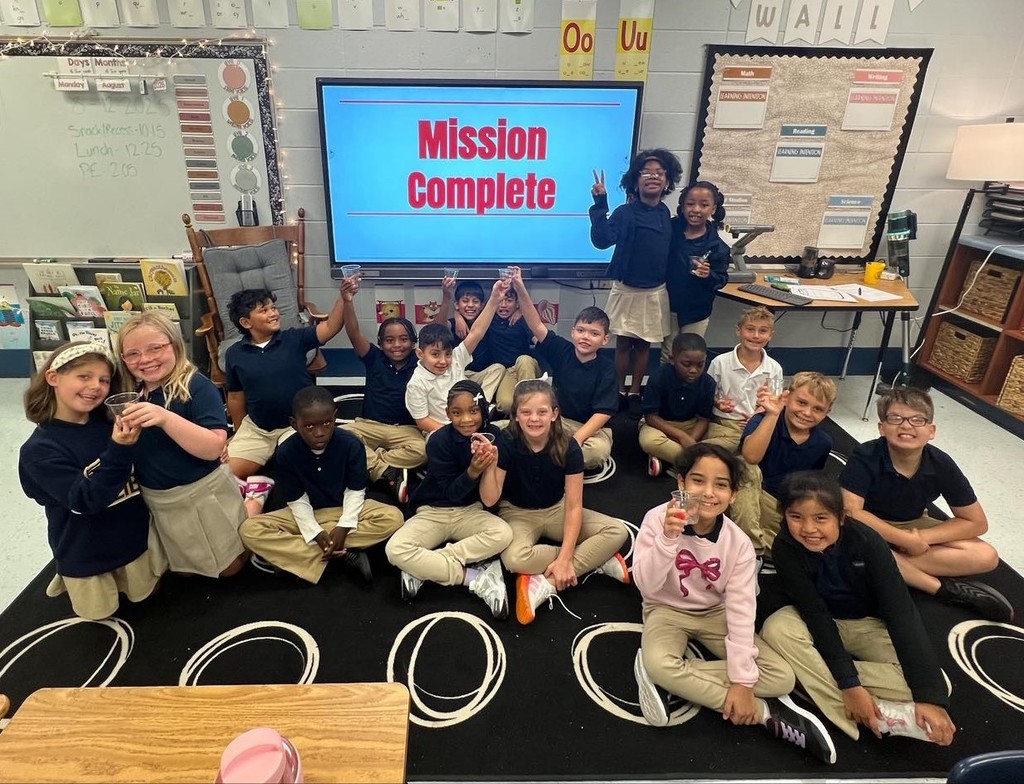 A group of students sitting in front of a smart board that reads "mission complete"