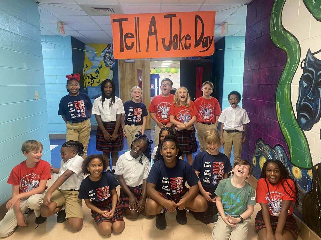 A group of students laughing in a hallway beneath a banner that reads "Tell a Joke Day"