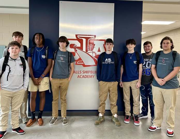 Eight high school boys standing in front of a sign that says "Ingalls Shipbuilding Academy"
